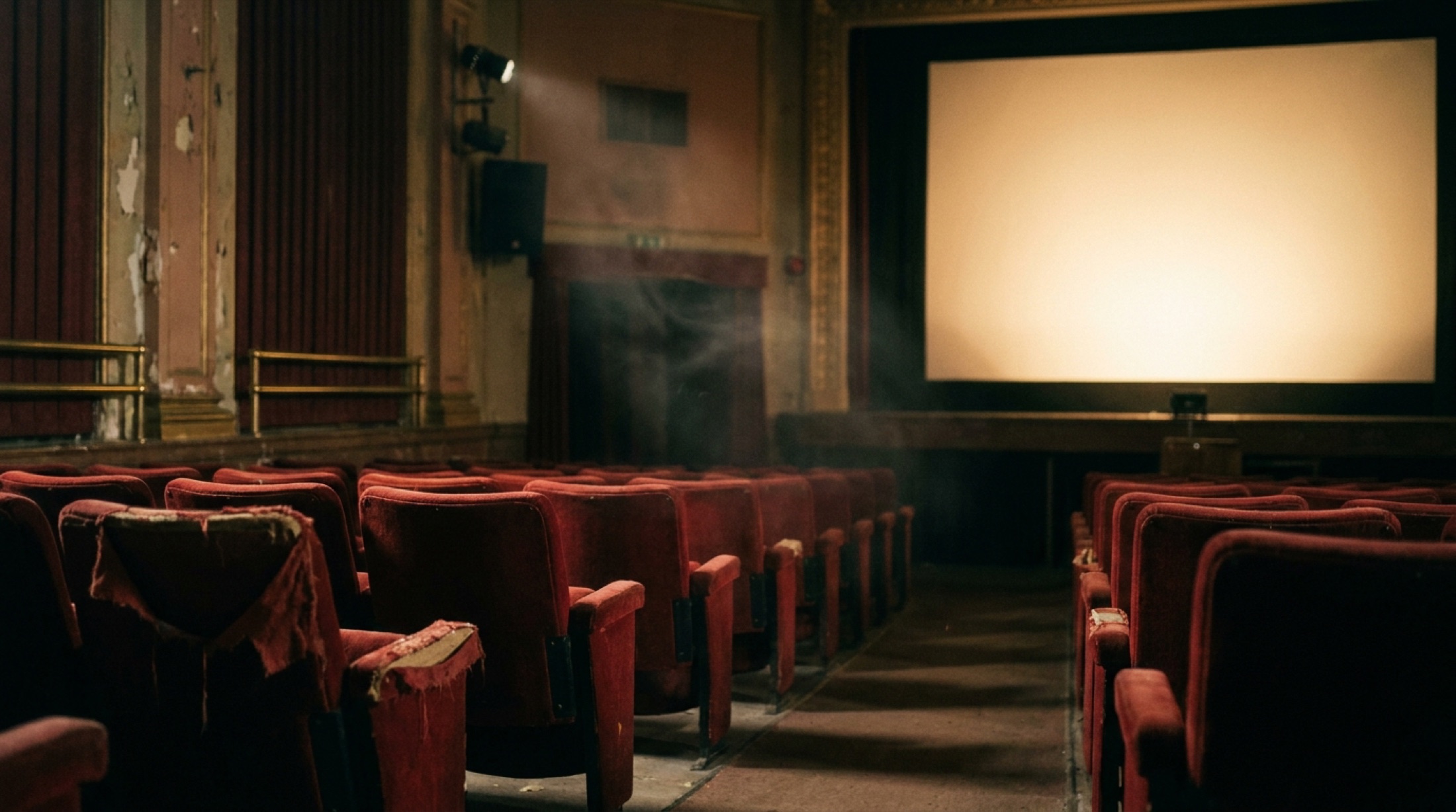 Loş ışıkta, boş kırmızı kadife koltuklar ve parlayan bir sinema perdesi