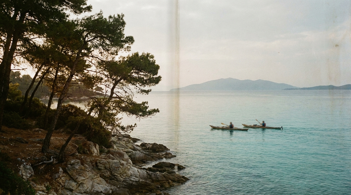 Vourvourou kıyısından bir görünüm; çam ağaçlarıyla çevrili sakin bir plaj, denizde birkaç kano, uzakta Diaporos adası.